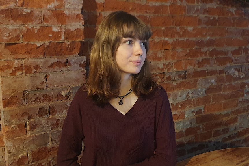 A girl sits in front of a brick wall