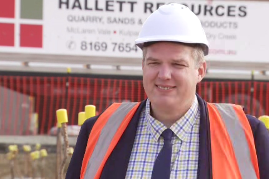 A middle-aged man in a white hardhat wearing a high-visibility vest. 