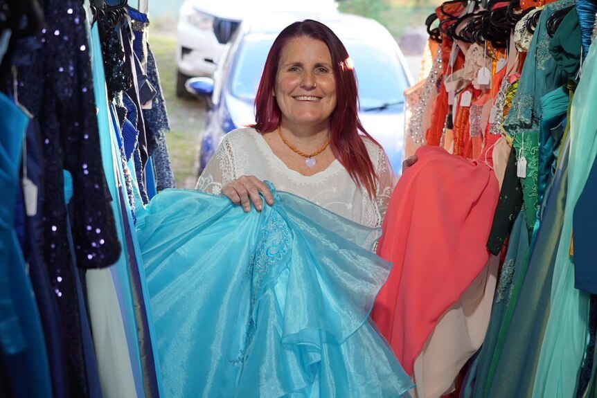 Tammy Robinson smiles as she stands with donated formal wear.