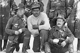 An Aboriginal man wearing a grey shirt surrounded by other men in army uniform standing in snow.