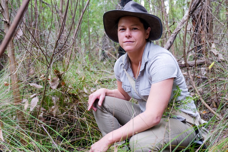 A woman crouching in the bush smiling at the camera.