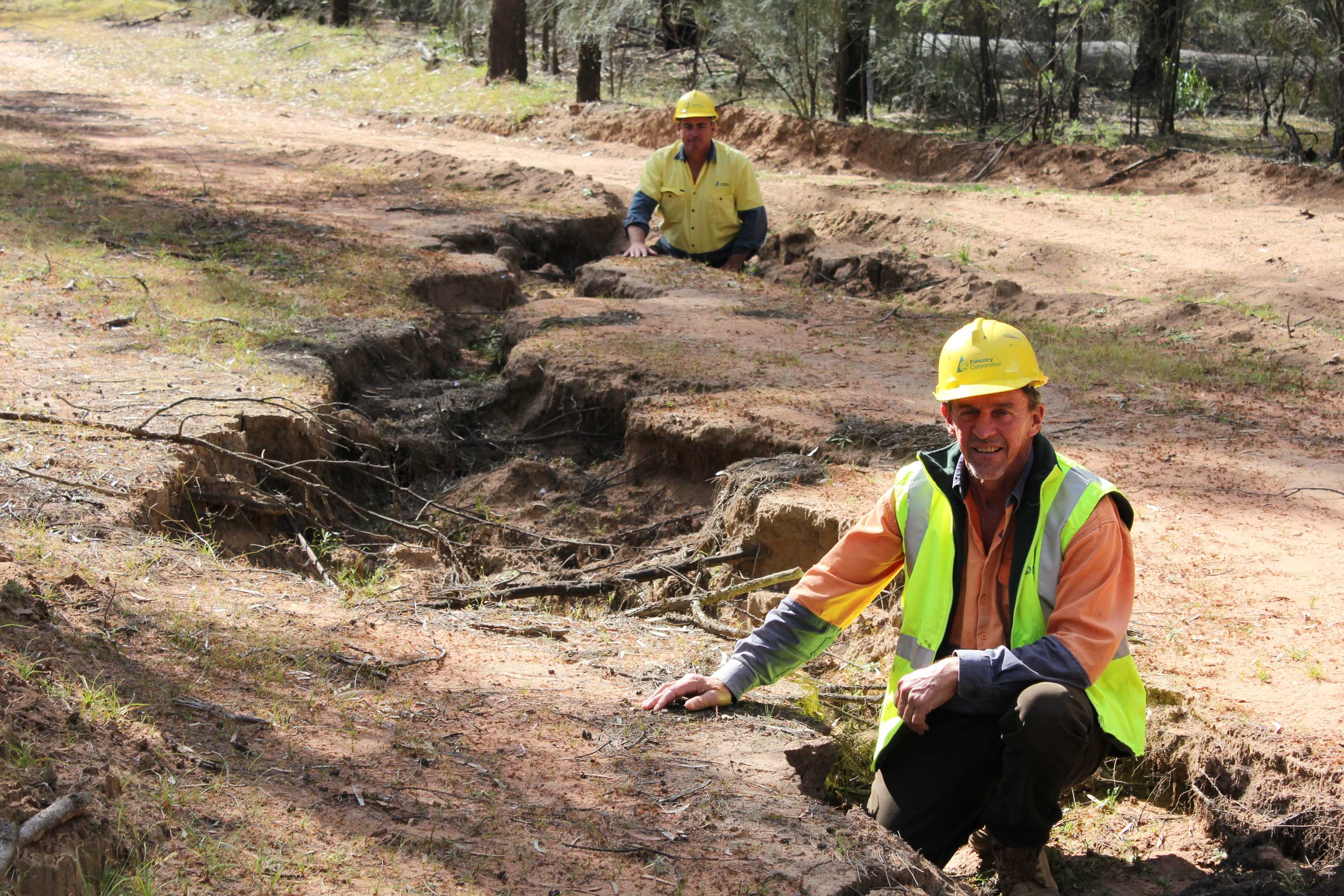 Two men squatting inside a deep earthen hole.