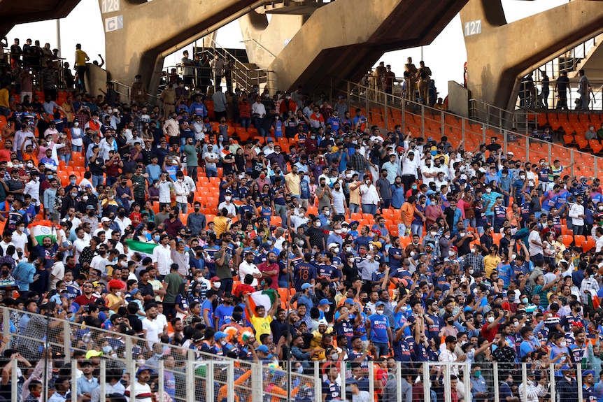 A huge crowd in a stadium with bright orange seats.