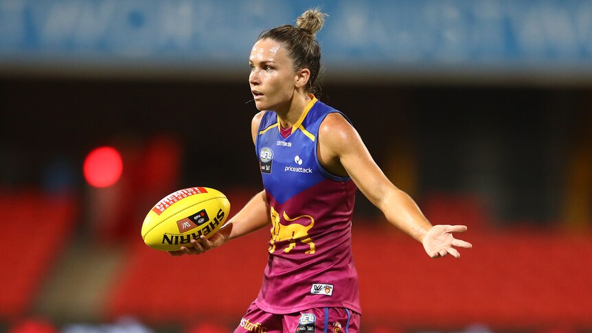 Brisbane Lions AFLW player Emily Bates shrugs as she holds a football.