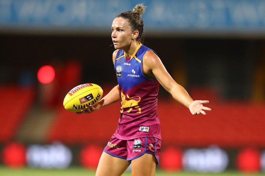Brisbane Lions AFLW player Emily Bates shrugs as she holds a football.