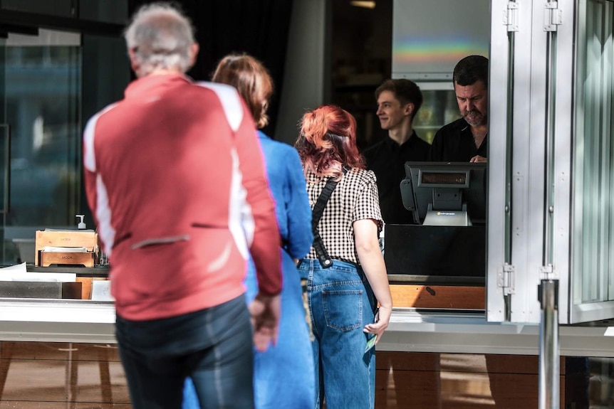 Three people line up outside a Brisbane cafe and a man serves the front customer.