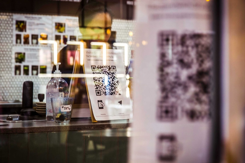 a woman behind a glass window with a qr code printed on a paper standing in front of her
