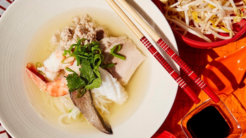 Phnom Penh noodle soup (Hủ tiếu Nam Vang) on woven platter with bean sprouts, sauces and chopsticks.