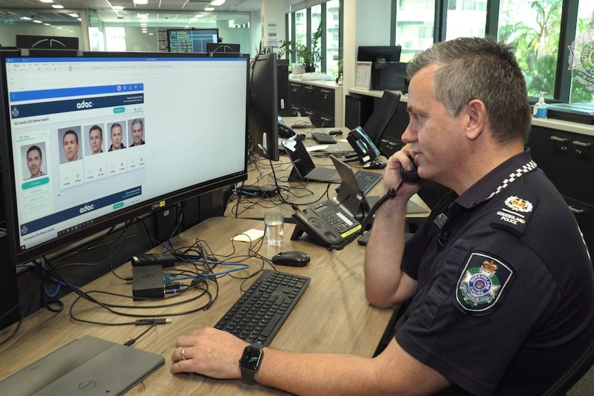 police officer on phone looking at faces on a computer