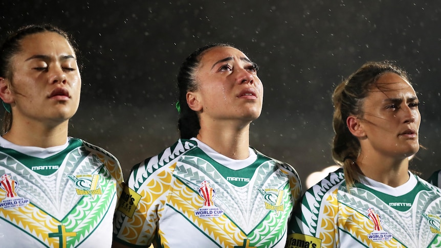 库克群岛球员贾兹蒙·图普-巫婆站着哭泣和她的队友一起参加女子橄榄球联赛世界杯。” class=