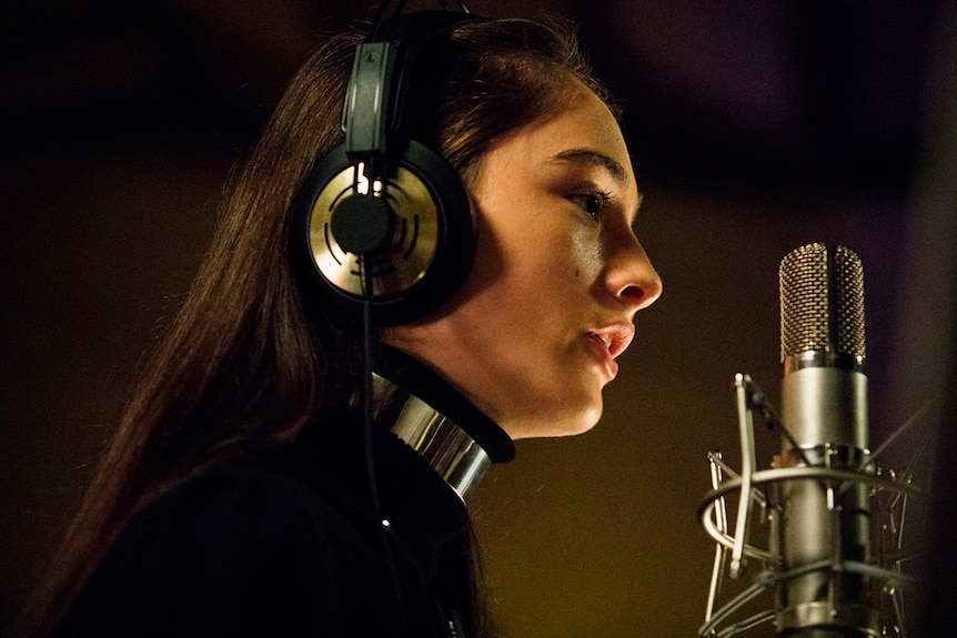 Close-up colour still of Raffey Cassidy singing in recording studio in 2018 film Vox Lux.