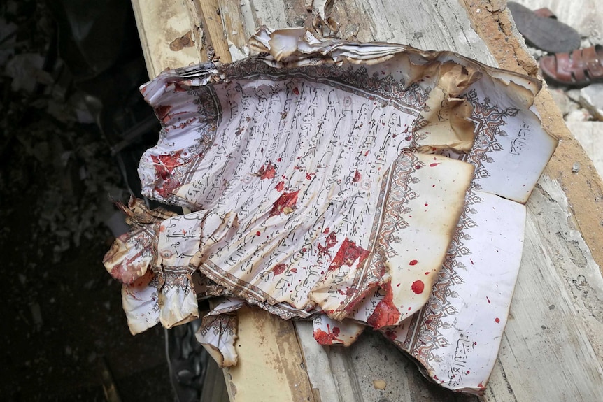 A partially burnt page of Koran is stained with blood