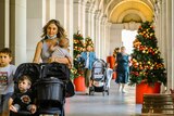 A mother walks with three children and a pram through an archway at the General Post Office, with Christmas tree.