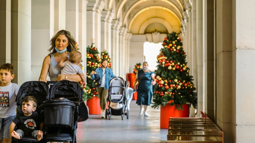 A mother walks with three children and a pram through an archway at the General Post Office, with Christmas tree.