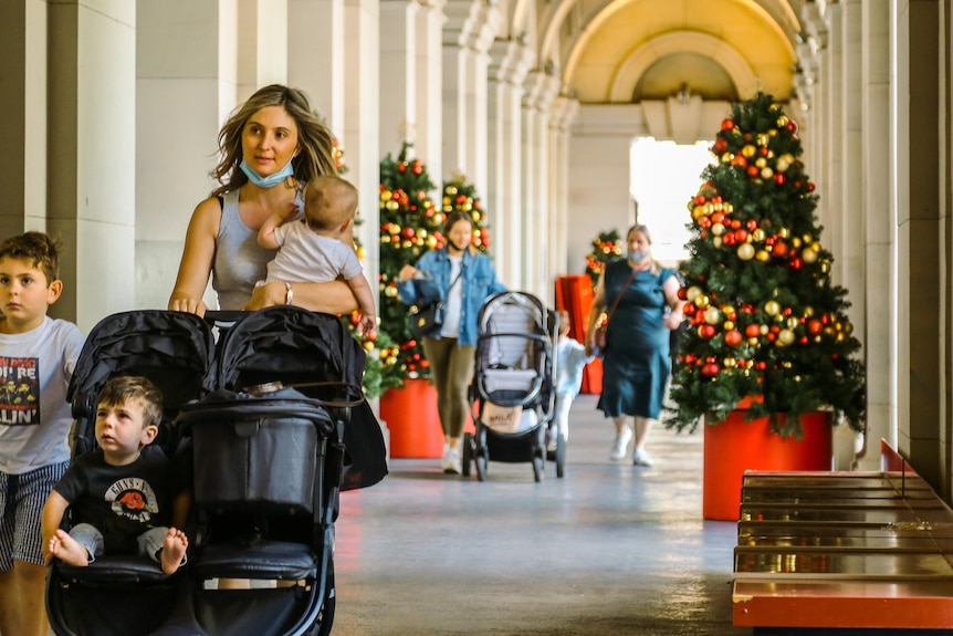 A mother walks with three children and a pram through an archway at the General Post Office, with Christmas tree.