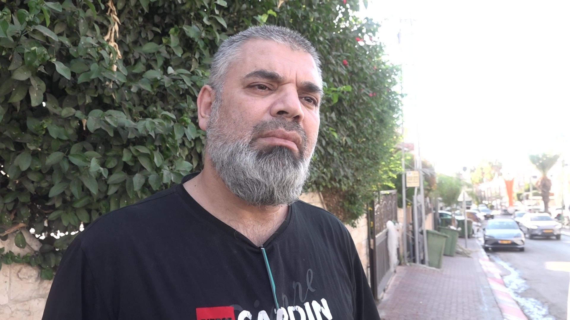 A man with a a white beard standing in front of a bush.