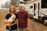 Lisa and James Bartlett hold a small dog outside a caravan.
