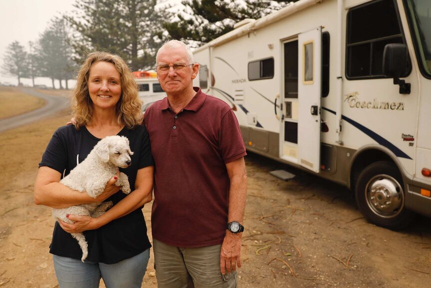 Lisa and James Bartlett hold a small dog outside a caravan.