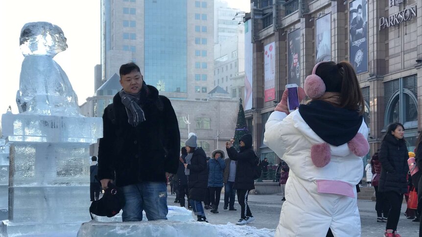 Woman takes picture of man standing next to an ice sculpture.