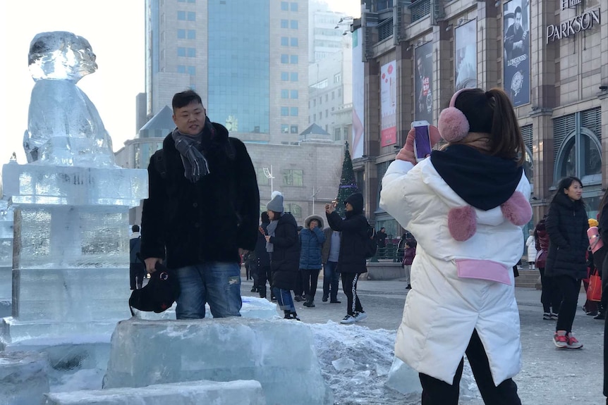 Woman takes picture of man standing next to an ice sculpture.