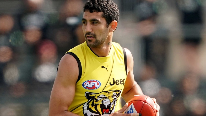 Marlion Pickett holds the ball in both hands wearing a yellow tigers training singlet