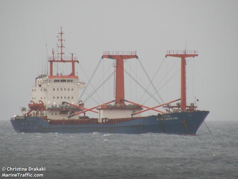 A red white and blue cargo ship floating in the ocean with thick white fog in the distance.