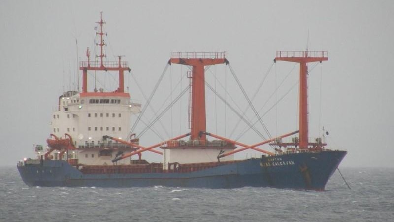 A red white and blue cargo ship floating in the ocean with thick white fog in the distance.