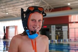 A young man stands in front of a pool with a mask and snorkel on his head