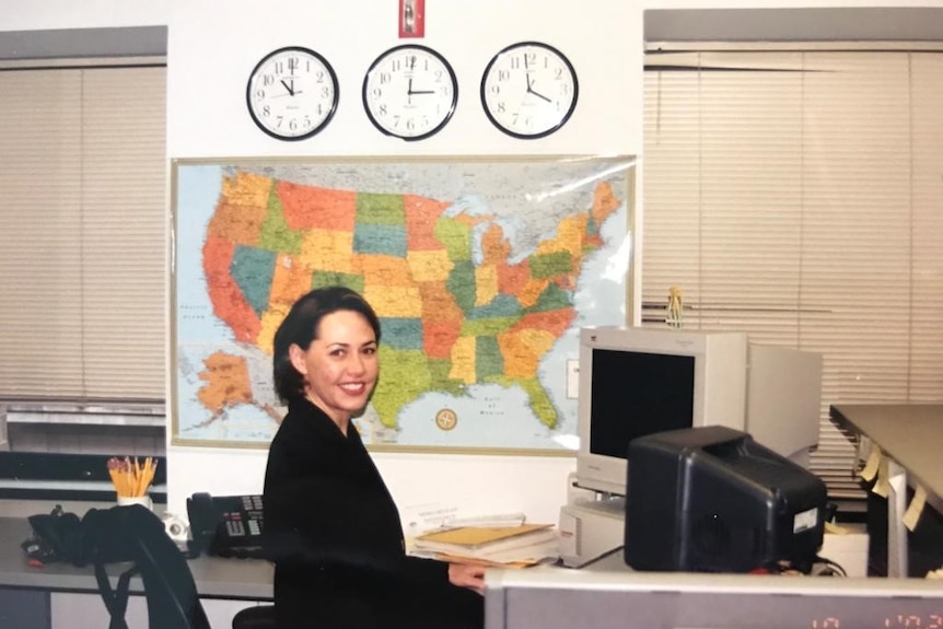 Woman sitting at desk with old fashioned computer and map of USA and clocks on wall.