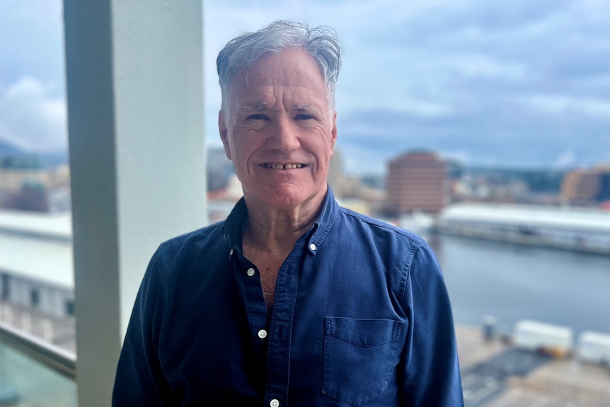 Older man wearing a blue button down shirt smiling. 