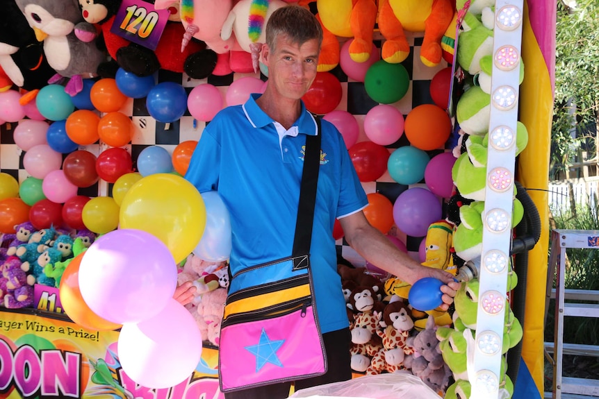 A store holder at the Ekka stands among balloons and plush toys.