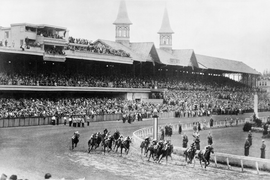 A black and white photograph of the Kentucky Derby in 1945, with the field going around a bend on track