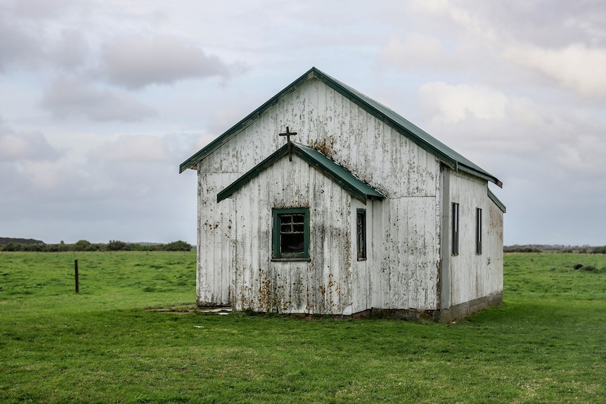 An old small wooden church on the roadside with decaying timber set among pastures