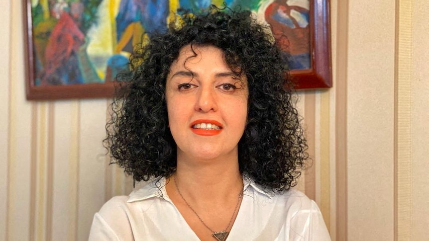 Woman with black curly hair smiles in front of wall with colourful painting. 