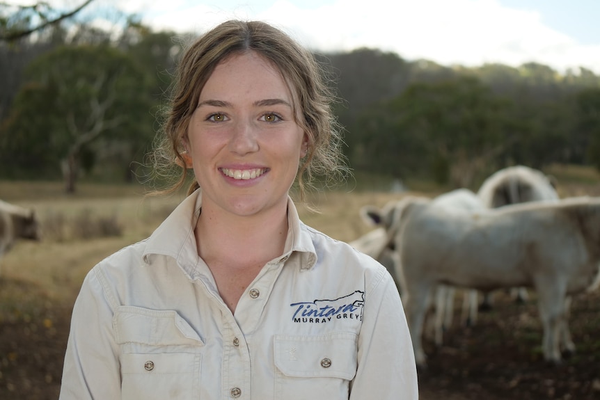 A young girl stands smiling at the camera with cows behind her.