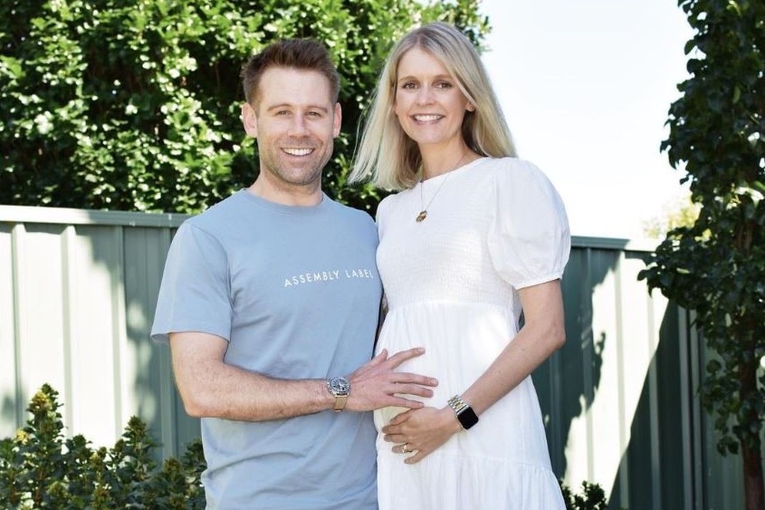Dr Michela Sorensen standing with her husband and dog, their hands on her pregnancy bump