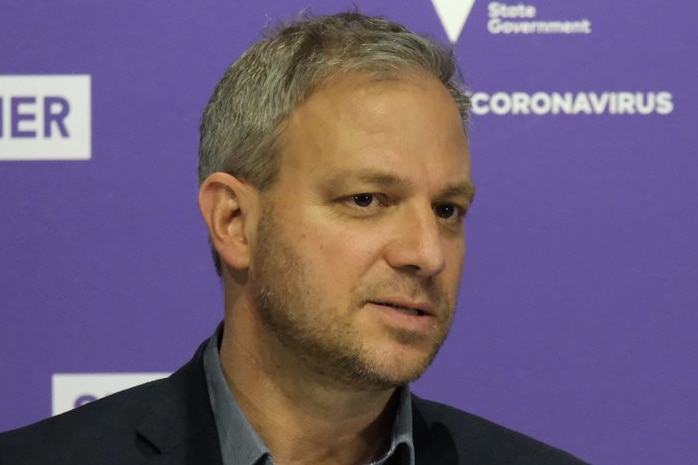 Brett Sutton stands at a lectern in front of a purple health department background during the press conference.