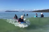 A group of older women on surfboards catch some waves.