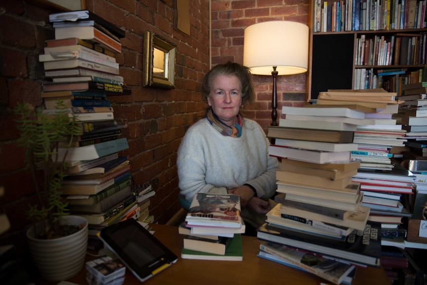 Rachel sits in front of a lamp, surrounded by piles of books