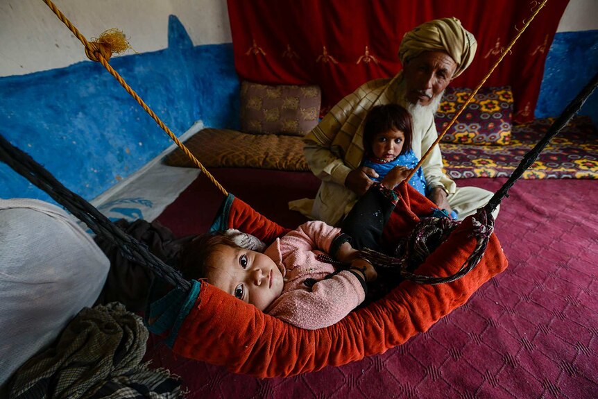 An older mans holds a young child while a baby lies in a makeshift crib in Afghanistan