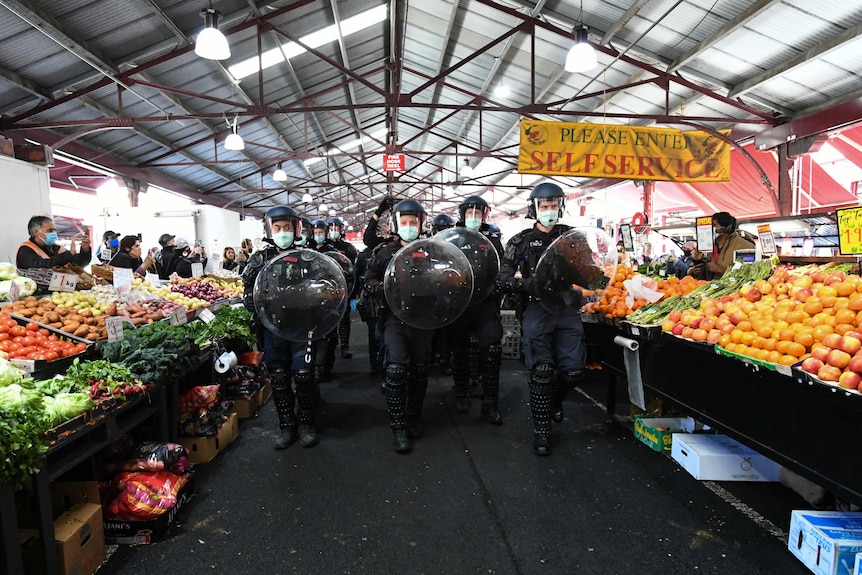 Police in riot gear walk down a fruit and vegetable aisle of the Queen Victoria Market.