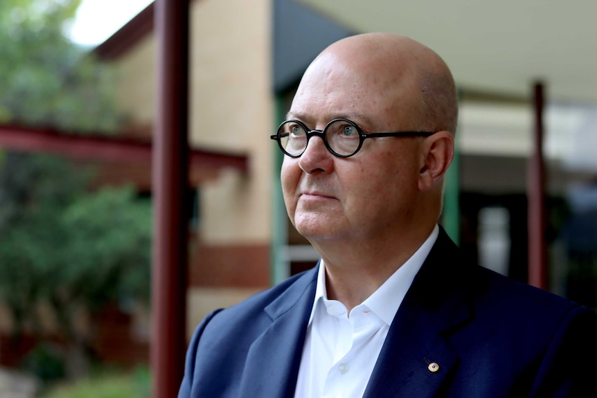 Kim Williams in a white shirt and a jacket stands outside a building.