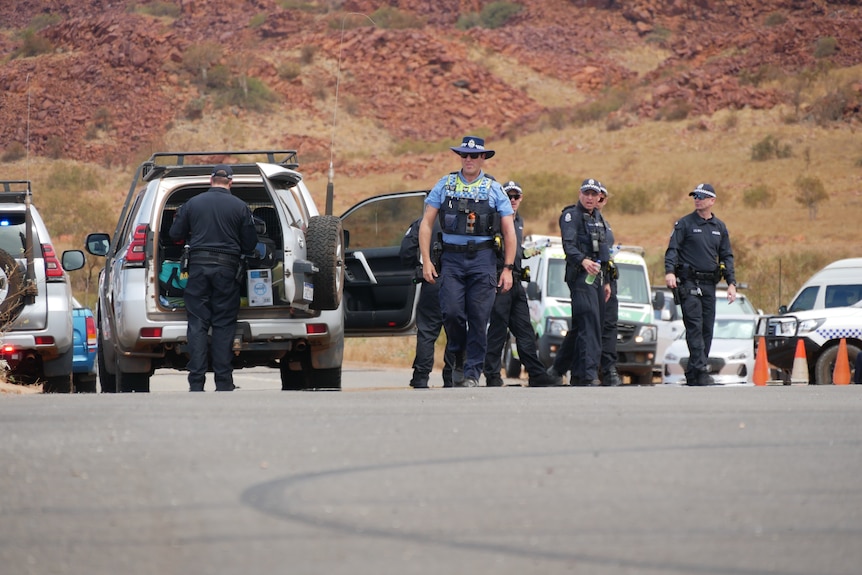 Multiple police and emergency vehicles and personnel on a road in the desert.