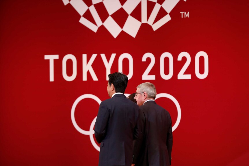 Two men walk with their backs to the camera against a red logo.