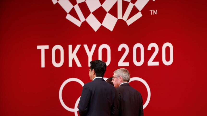 Two men walk with their backs to the camera against a red logo.