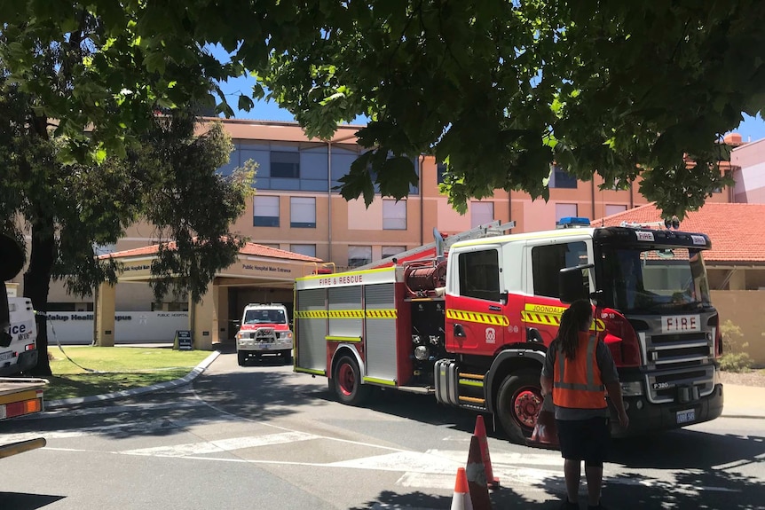 Two firetrucks outside Joondalup Health Campus, with a woman wearing high-vis in the foreground.