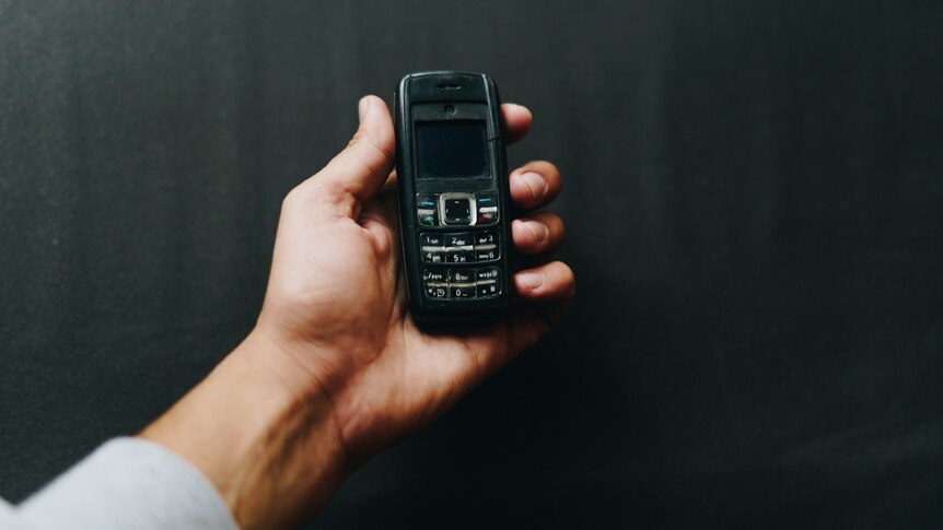 A man's hand holding an old mobile phone.