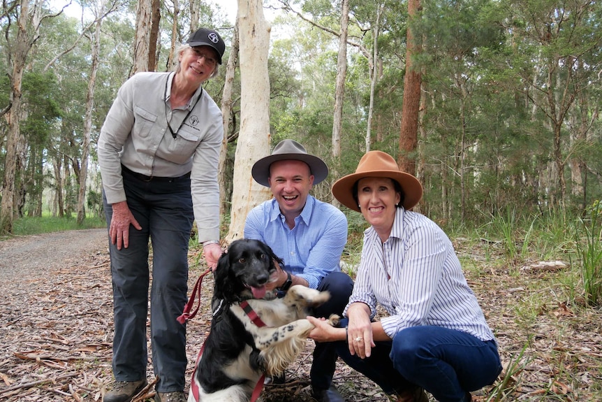 Three people smiling at a camera and a dog.