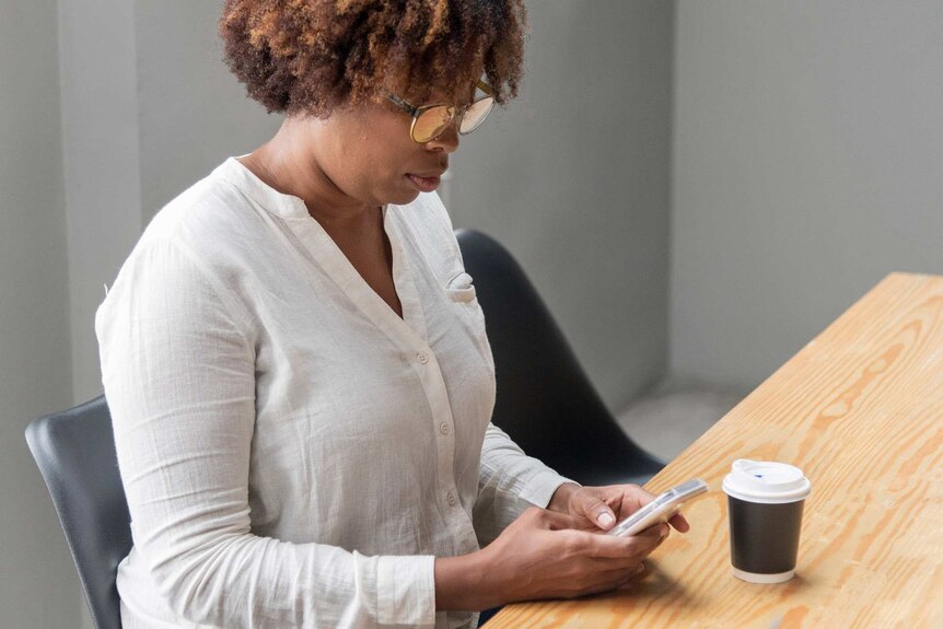 Woman on her phone in an office with a coffee cup next to her to depict how to deal with feeling lonely and isolated.