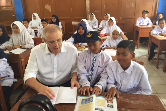 Scott Morrison at a desk with two Indonesian boys looking at a text book.
